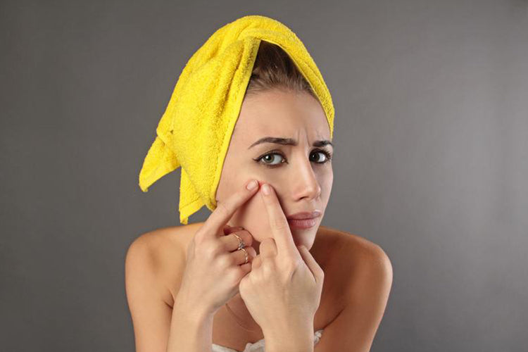 lady with a yellow towel in her hair squeezing a spot on her face